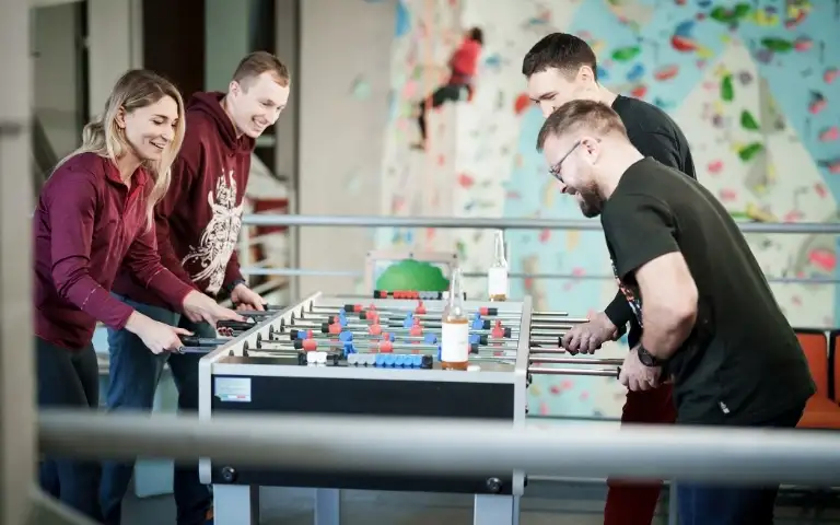 Grupa znajomych grająca w piłkarzyki z ścianą do wspinaczki w tle